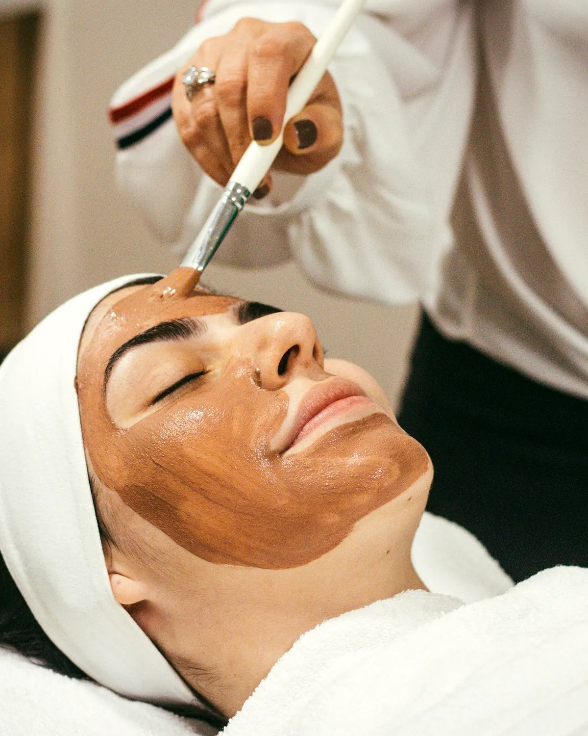 Masque à l’argile appliqué au pinceau sur une cliente détendue, les yeux fermés